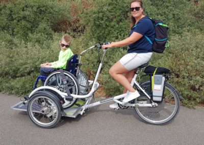 rolstoelfiets met rolstoel erop en begeleider fietst
